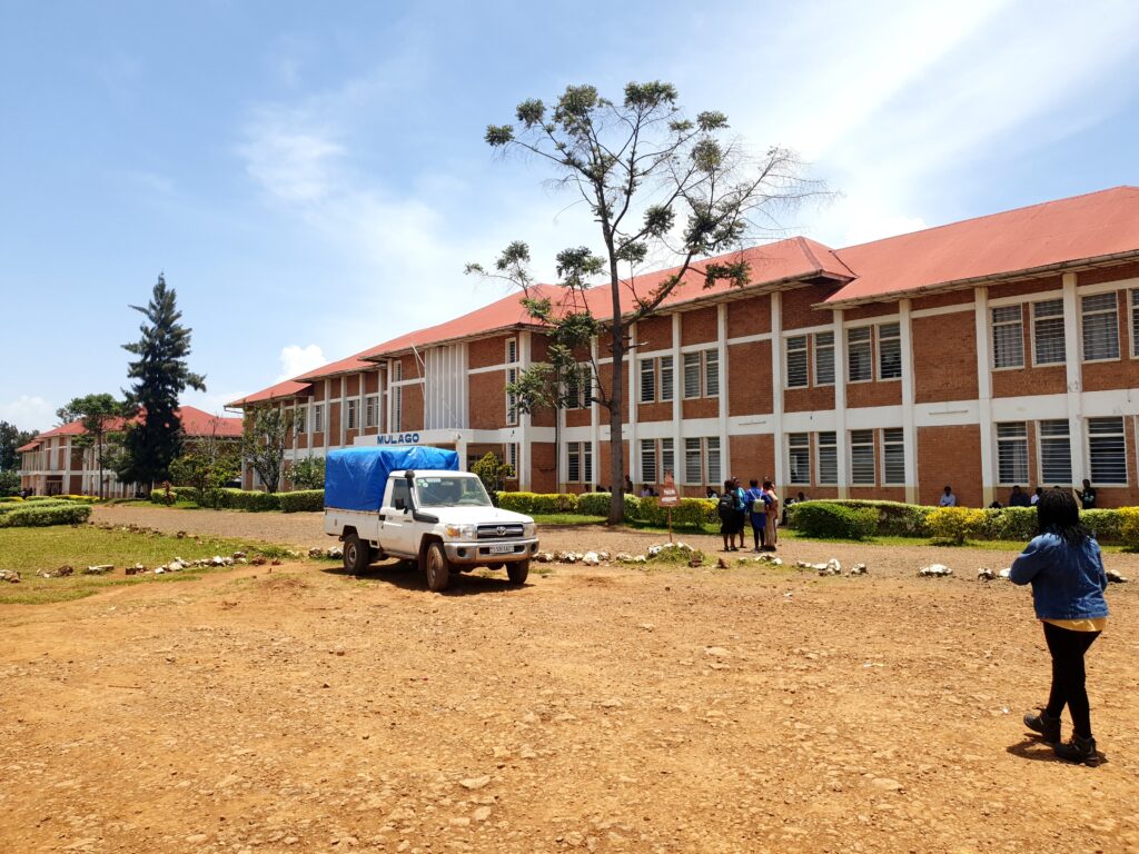 Deux bâtiments de l'Université Catholique de Bukavu, sur le site de Kalambo. Les étudiants marchent sous le ciel ensoleillé. Le sol est empoussiéré.