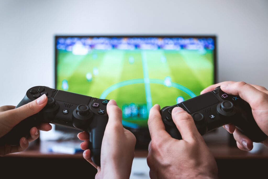 Deux manettes de PlayStation et un écran. Deux personnes qui jouent à un jeu de sport. Du terrain aux écrans : ma relation avec le sport.