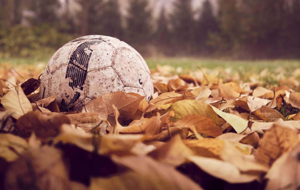 Ballon de football sur un tas de feuilles mortes. Du terrain aux écrans : ma relation avec le sport.